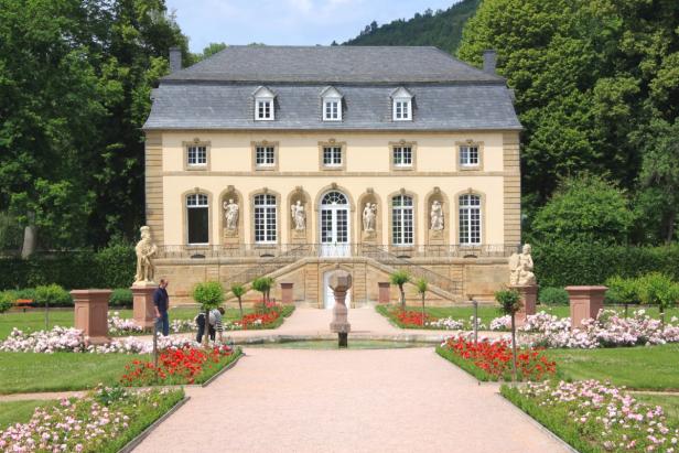 Ein Schloss mit einem formellen Garten und Statuen im Vordergrund.