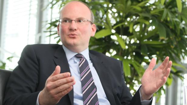 Ein Mann mit Brille und Anzug gestikuliert während eines Gesprächs.