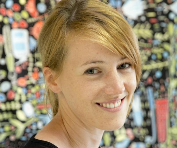 Eine lächelnde Frau mit blonden Haaren vor einem bunten Hintergrund.