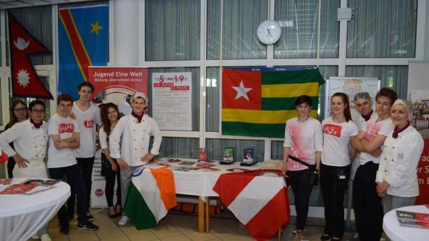 Eine Gruppe von Jugendlichen steht vor Flaggen verschiedener Länder und einem Banner von „Jugend Eine Welt“.