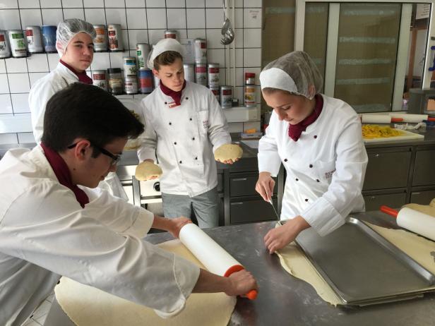 Vier junge Köche bereiten Teig in einer Küche zu.