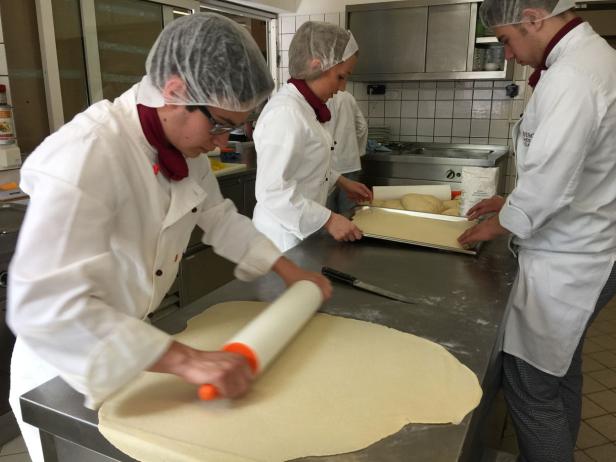 Drei Personen in Kochkleidung bereiten Teig in einer Küche zu.