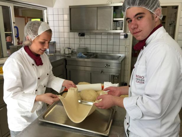 Zwei Köche in einer Küche bereiten Teig auf einem Backblech zu.