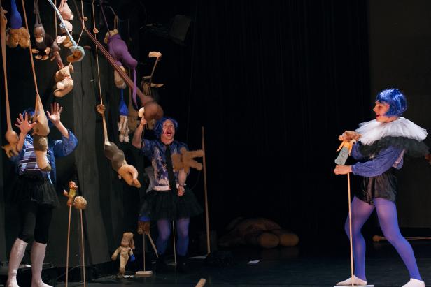 Eine Theaterszene mit drei Darstellern und zahlreichen Stofftieren.