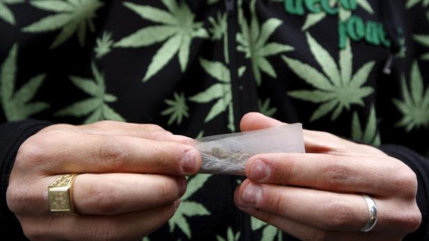 Eine Person rollt eine Zigarette mit Cannabis, bekleidet mit einem Hoodie mit Cannabisblatt-Muster.