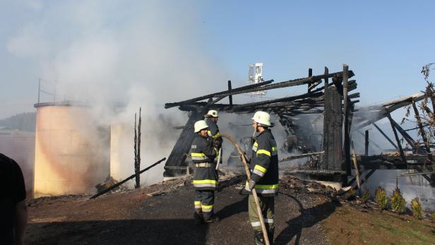 Drei Feuerwehrleute stehen vor den Überresten eines abgebrannten Gebäudes.