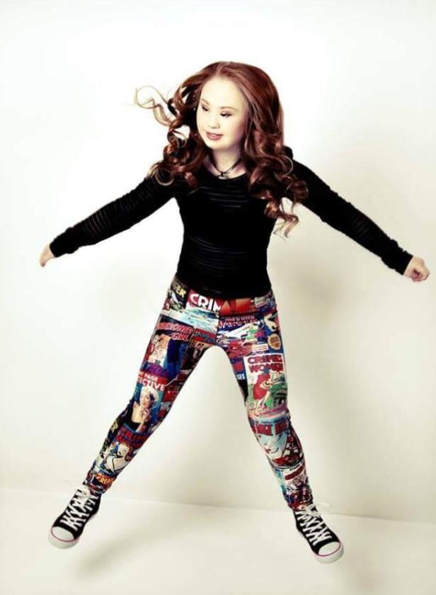 Eine junge Frau mit Down-Syndrom springt mit ausgestreckten Armen und Comic-Leggings.