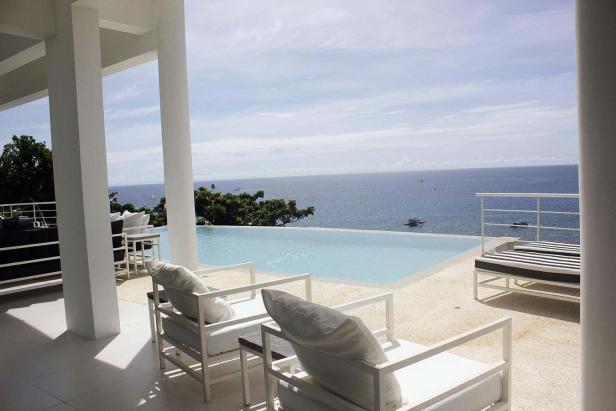 Ein Infinity-Pool mit Blick auf das Meer von einer Terrasse mit weißen Möbeln.