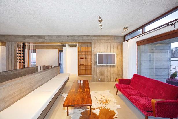 Ein Wohnzimmer mit Betonwänden, einem roten Sofa und einem Holztisch auf einem Kuhfellteppich.