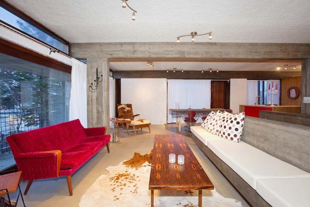 Ein Wohnzimmer mit Betonwänden, einem roten Sofa und einem Kuhfellteppich.