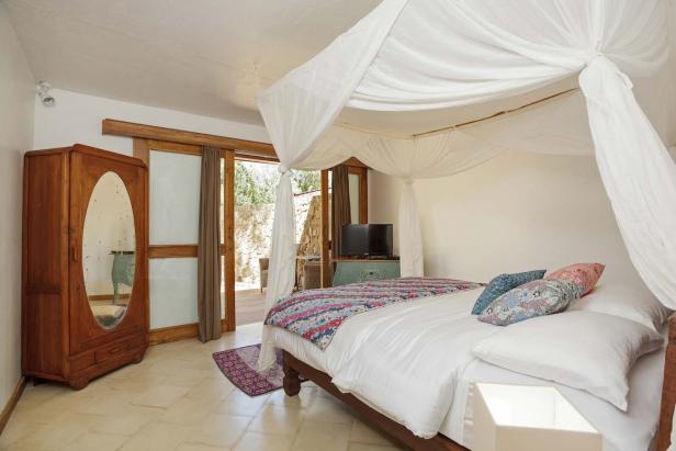 Ein Schlafzimmer mit Himmelbett, Holzkleiderschrank und Zugang zu einer Terrasse.