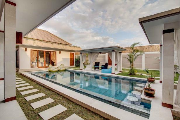 Ein rechteckiger Pool mit Liegen und einem Pavillon in einem tropischen Garten.