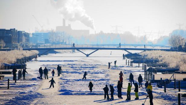 Auf einem zugefrorenen Kanal laufen Menschen Schlittschuh.