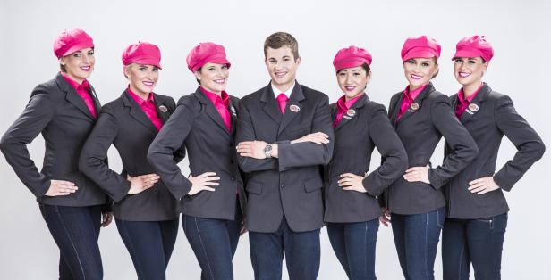 Eine Gruppe von Flugbegleitern und einem Flugbegleiter der Fluggesellschaft NIKI in Uniformen und pinkfarbenen Hüten.