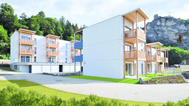 Ein modernes Mehrfamilienhaus mit Holzbalkonen vor einer bewaldeten Hügellandschaft.