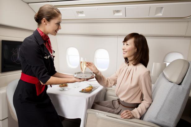 Eine Flugbegleiterin serviert einer Passagierin ein Glas Champagner im Flugzeug.