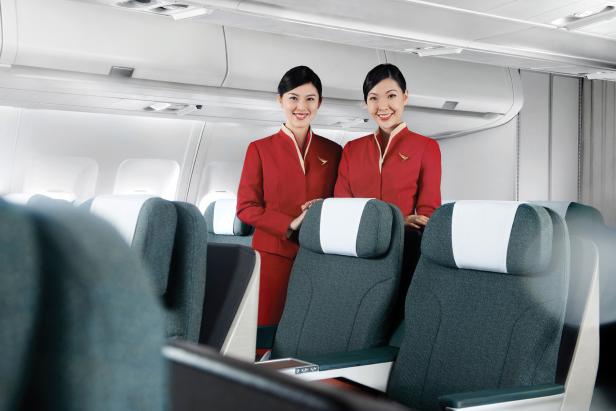 Zwei lächelnde Flugbegleiterinnen in roter Uniform in einem Flugzeug.