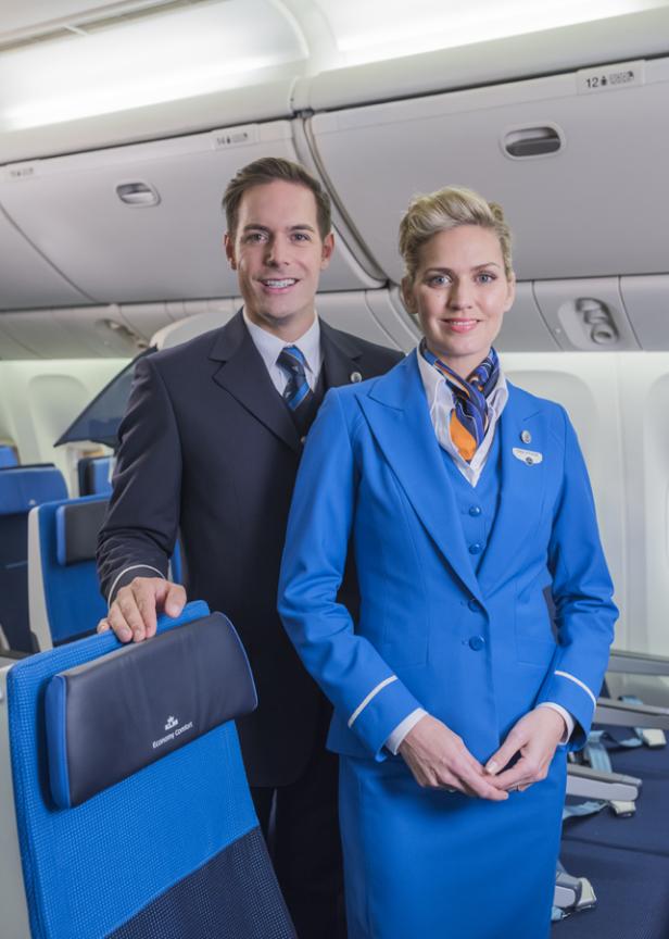 Ein Steward und eine Stewardess der KLM posieren in der Economy Comfort Class eines Flugzeugs.