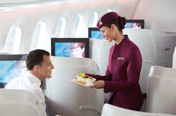 Eine Stewardess von Qatar Airways serviert einem Passagier in der Business Class Speisen.