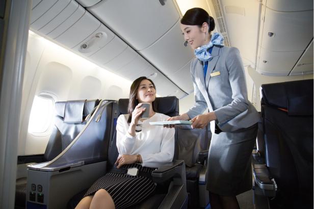 Eine Flugbegleiterin serviert einer Passagierin ein Getränk im Flugzeug.