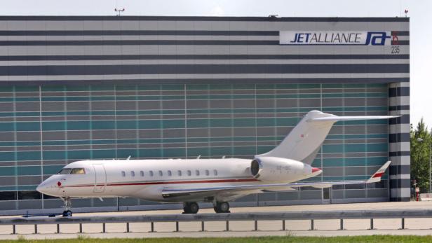 Ein weißes Privatflugzeug steht vor einem Hangar von Jetalliance.