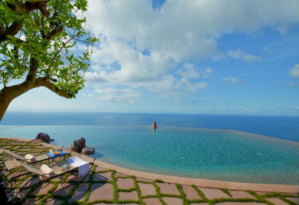 Eine Frau schwimmt in einem Infinity-Pool mit Blick auf das Meer.
