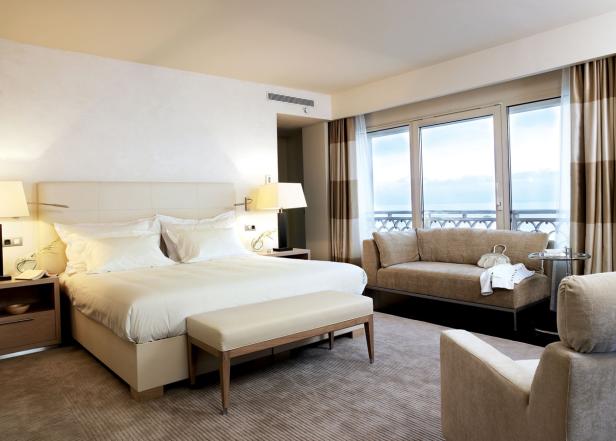 Ein helles Hotelzimmer mit Doppelbett, Sofa und Blick auf das Meer.