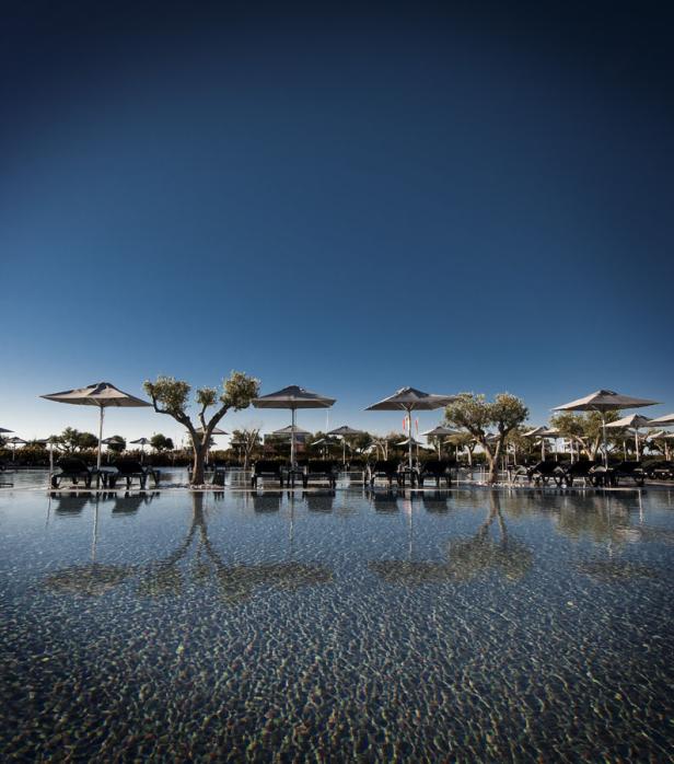 Ein Schwimmbad mit Liegestühlen und Sonnenschirmen unter einem blauen Himmel.