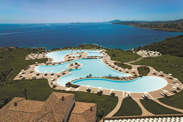 Ein großer Poolkomplex mit Liegestühlen und Sonnenschirmen liegt an der Küste mit Blick auf das Meer.