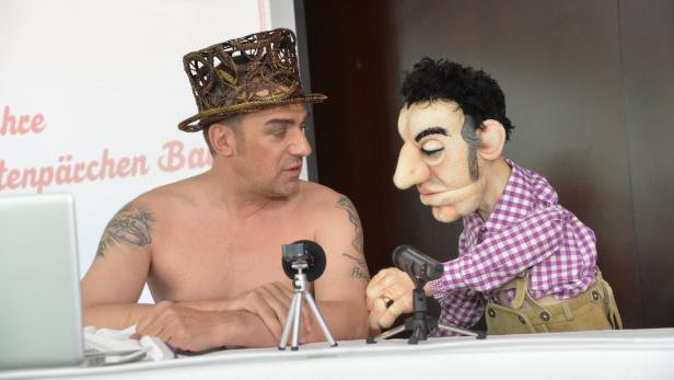 Ein Mann mit Hut und eine Puppe stehen vor zwei kleinen Kameras.