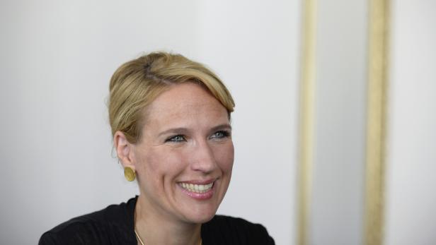 Eine lächelnde Frau mit blonden Haaren und goldenen Ohrringen.