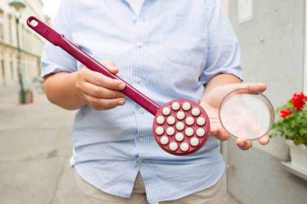 Eine Person hält einen Rückenmassagegerät und eine durchsichtige Dose in der Hand.