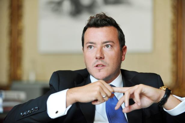 Ein Mann im Anzug mit gepunkteter Krawatte gestikuliert mit den Händen.