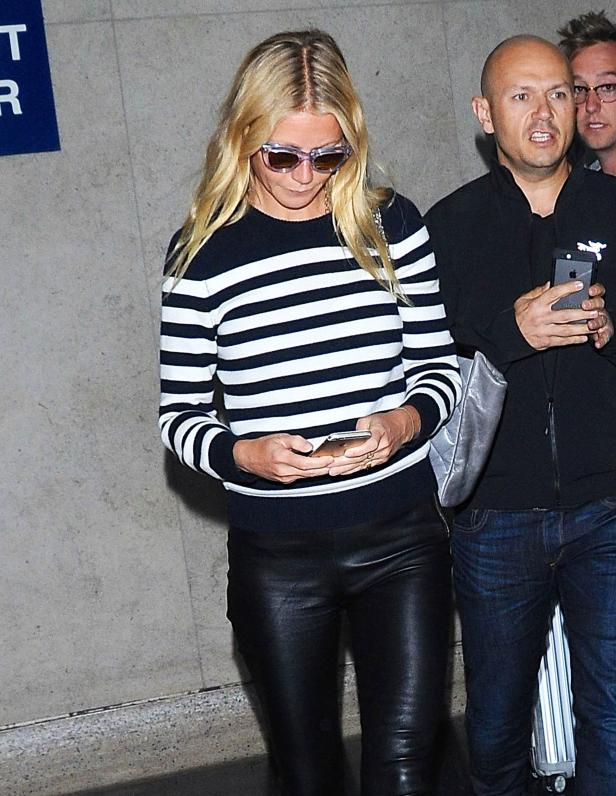 Eine blonde Frau mit Sonnenbrille und gestreiftem Pullover schaut auf ihr Handy.