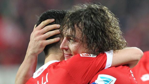 Zwei Fußballspieler in roten Trikots umarmen sich auf dem Spielfeld.