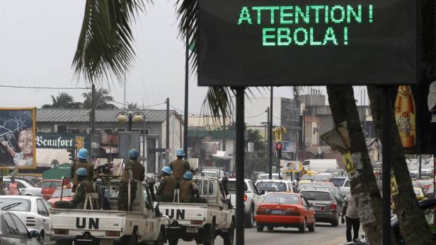 UN-Friedenstruppen patrouillieren in einem belebten Stadtgebiet mit einer Ebola-Warnung im Hintergrund.