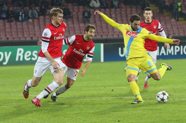 Ein Fußballspieler von Neapel schießt den Ball, während zwei Arsenal-Spieler zusehen.