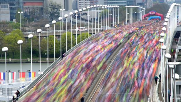 Ein Marathonlauf überquert eine Brücke, die mit vielen Menschen gefüllt ist.