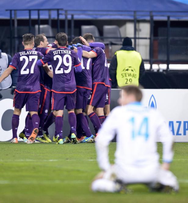 Eine Gruppe Fußballspieler in lila Trikots umarmt sich, während ein Spieler im Vordergrund kniet.