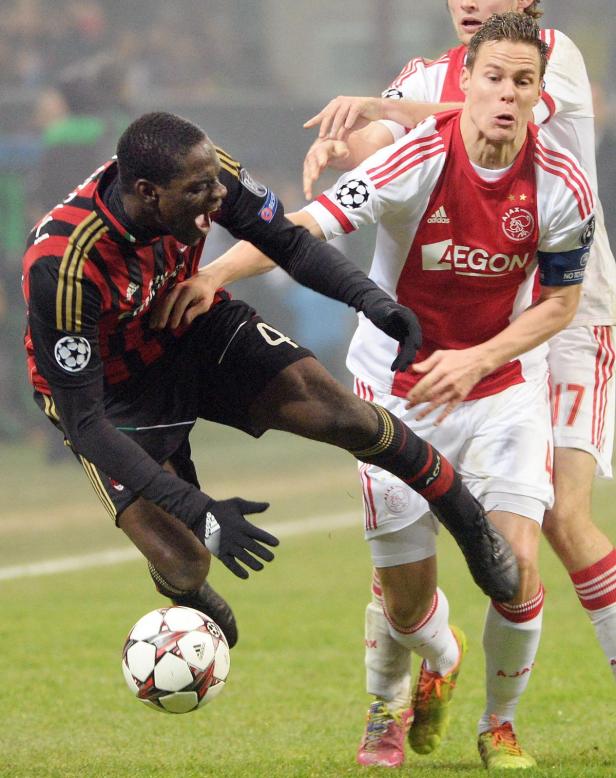 Ein Fußballspieler von AC Mailand grätscht nach dem Ball, während ein Spieler von Ajax zusieht.