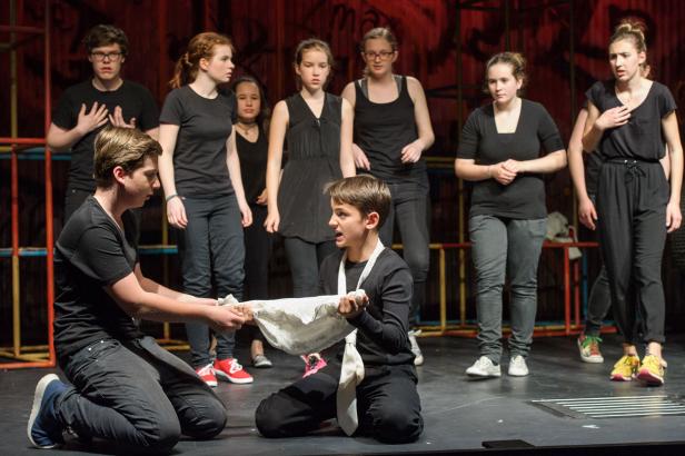 Zwei Jugendliche auf der Bühne ziehen an einem Tuch, während andere zusehen.