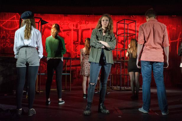 Eine Gruppe junger Leute steht auf einer Bühne vor einem roten Hintergrund.