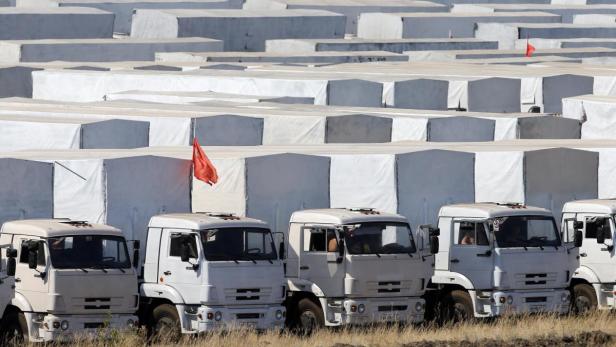 Mehrere weiße Lastwagen stehen vor einer Lagerhalle mit roten Flaggen.