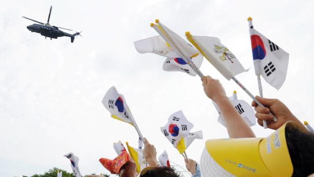 Menschen schwenken Flaggen Südkoreas und des Vatikans, während ein Hubschrauber am Himmel fliegt.