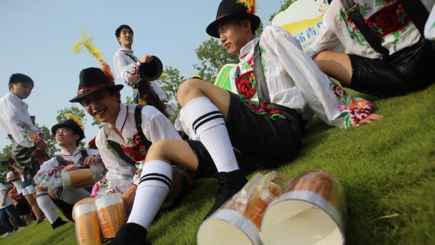 Eine Gruppe junger Männer in Tracht sitzt mit Bierkrügen auf einer Wiese.