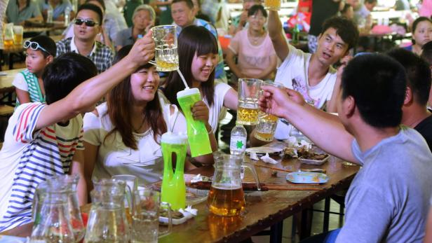 Eine Gruppe von Menschen stößt mit Bierkrügen an einem Tisch an.