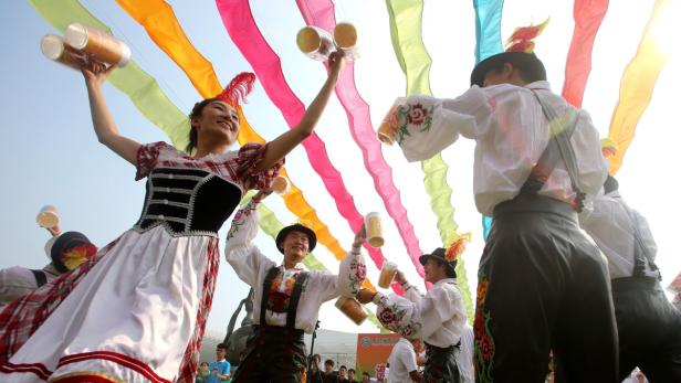 Menschen in Tracht tanzen mit Bierkrügen unter bunten Bändern.
