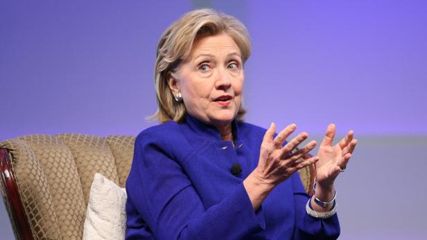 Hillary Clinton gestikuliert während einer Rede vor einem lila Hintergrund.