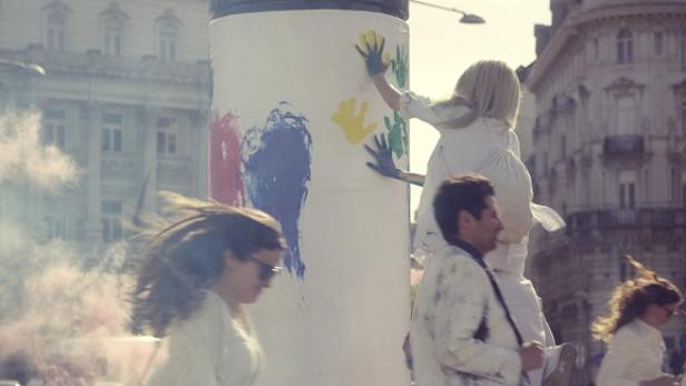 NÖM - Markenkampagne 2015 - TV-Spot Bild 15 Menschen bemalen eine Säule mit bunten Handabdrücken.