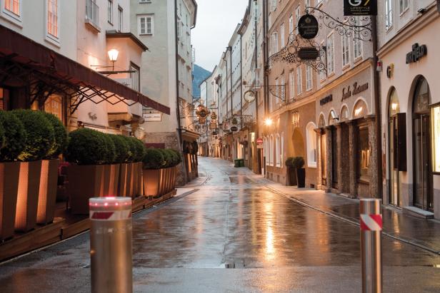 Eine regnerische Gasse in Salzburg mit spiegelndem Pflaster und historischen Gebäuden.